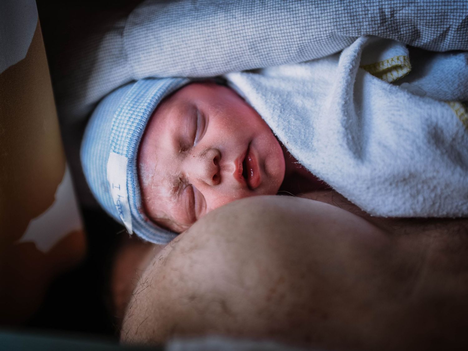 Newborn baby wearing a blue hat swaddled in a light blue towel resting peacefully after birth.