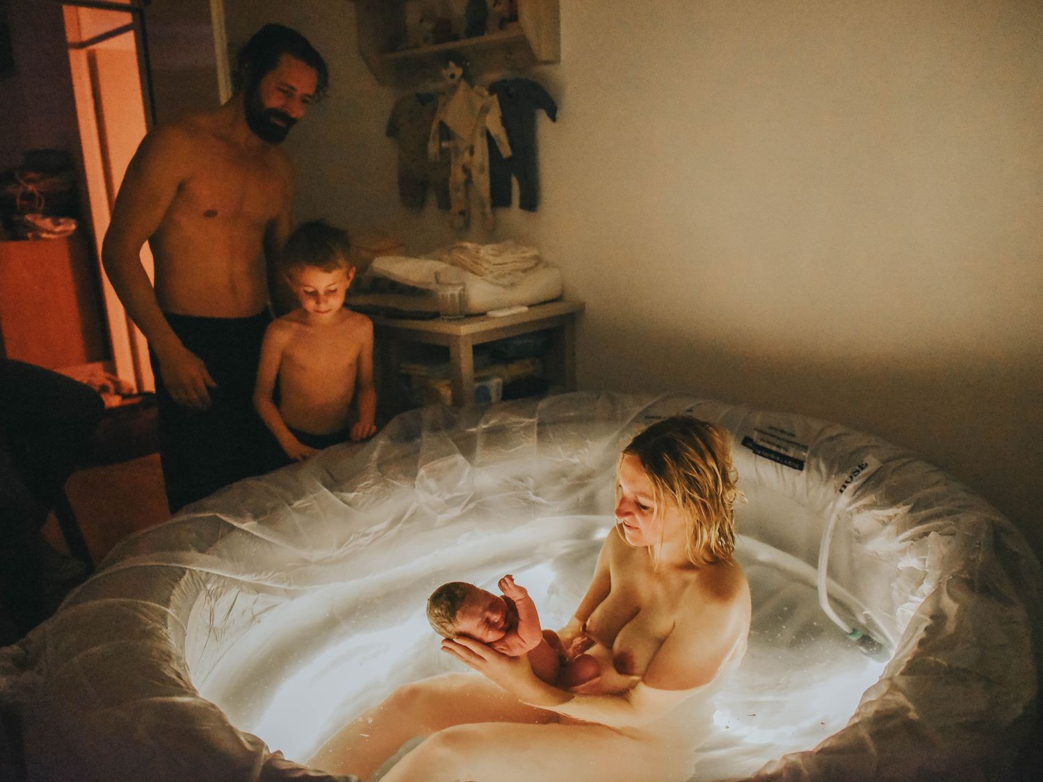 A family welcomes a newborn during a home water birth, with mother holding baby in a birthing pool.