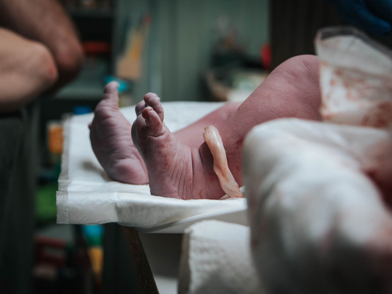 Close-up of a newborn baby's feet and legs moments after birth on a white hospital blanket.