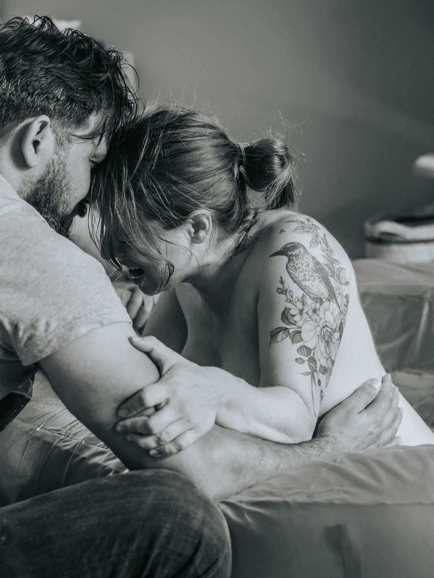 Black and white photo of a couple sharing an intimate moment, woman with floral bird shoulder tattoo.