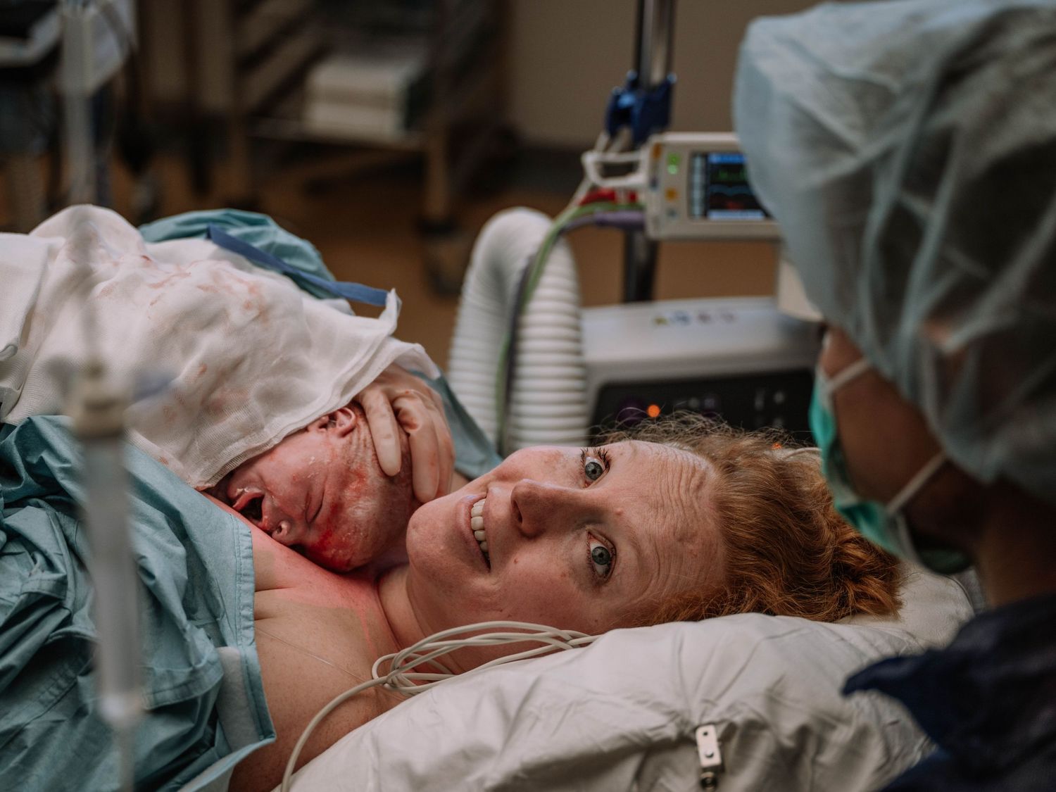 New mother smiling in hospital bed during skin-to-skin contact with newborn baby after delivery.