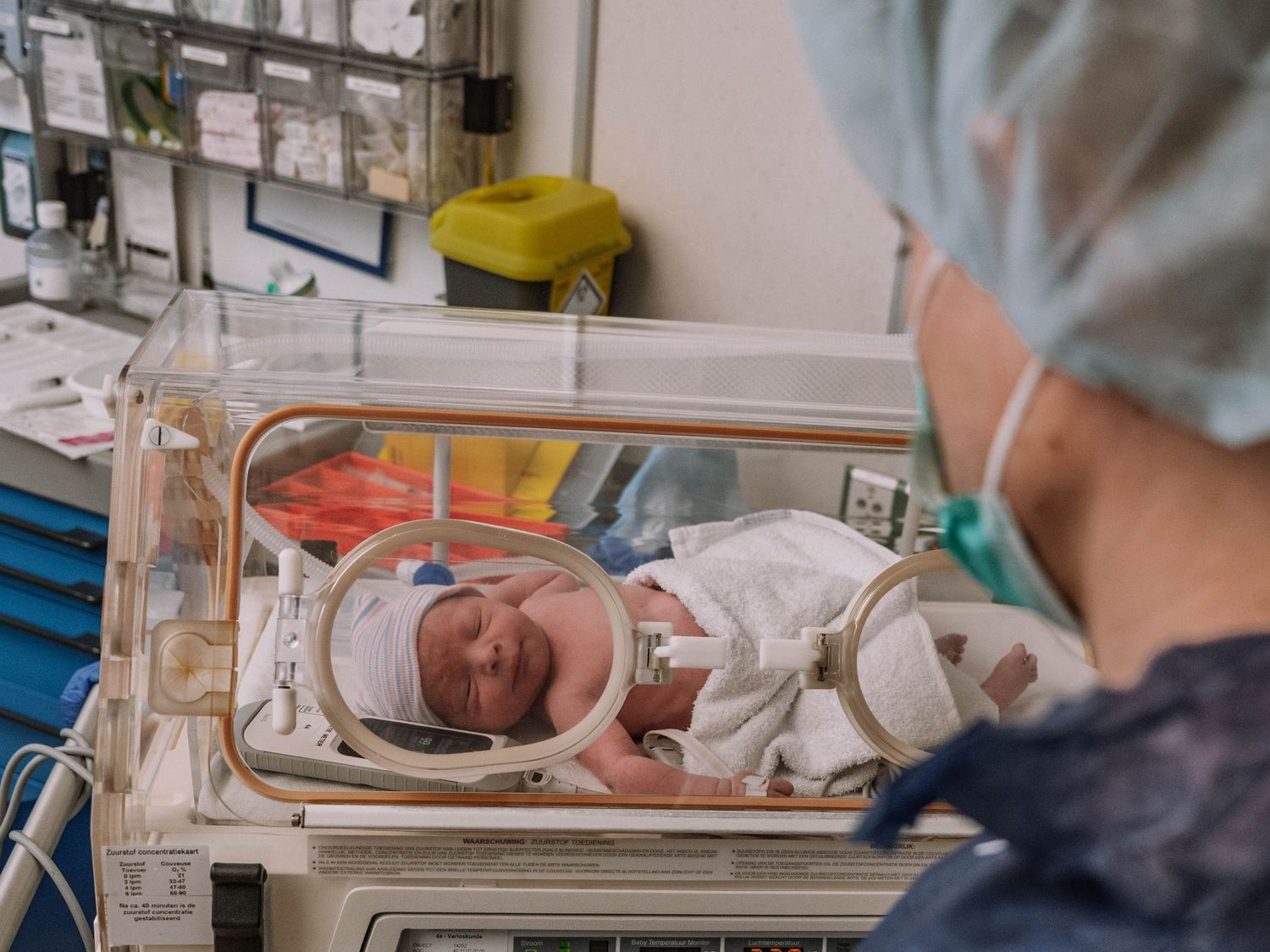 Premature newborn baby resting in a hospital incubator under medical supervision in a neonatal intensive care unit.