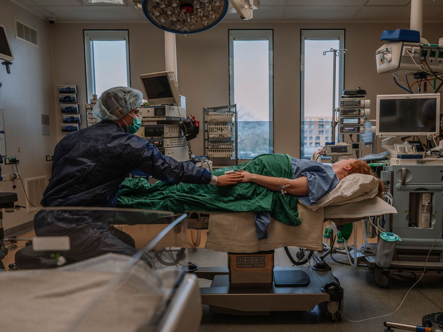 Medical professional in scrubs attending to a patient lying on an operating table in a modern hospital surgical room.