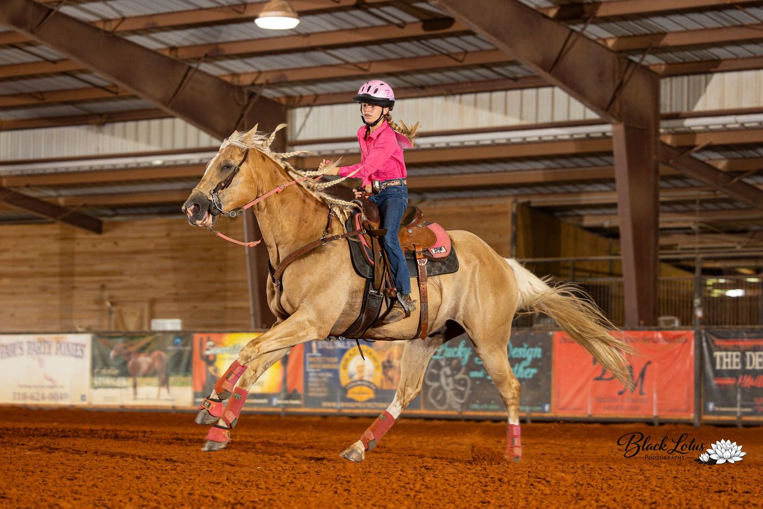 Young girl in pink outfit riding a palomino horse indoors at an equestrian arena competition event.