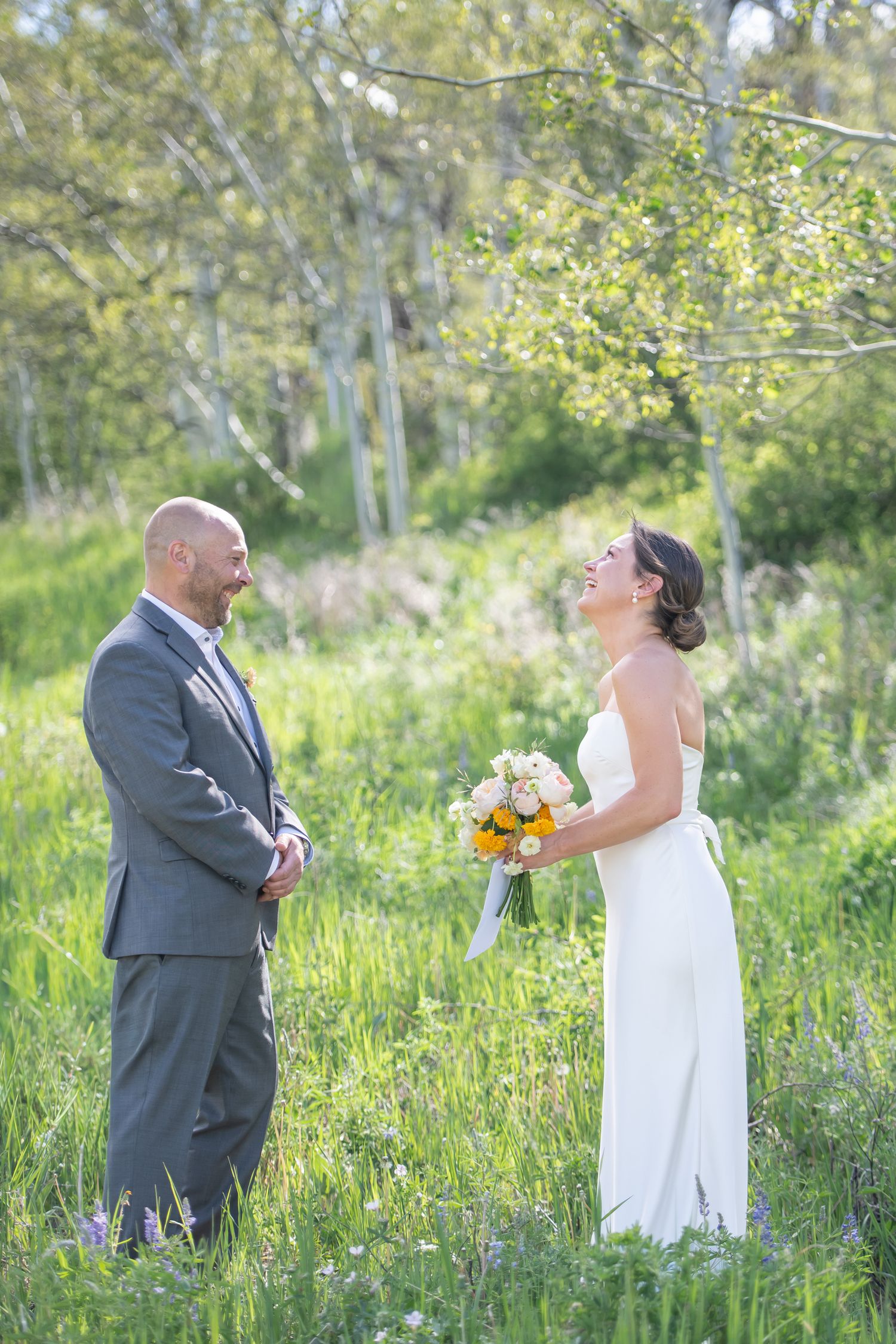 Bride and groom share a joyful first look moment in a lush green meadow, bride holding a colorful bouquet at Beaver Creek elopement