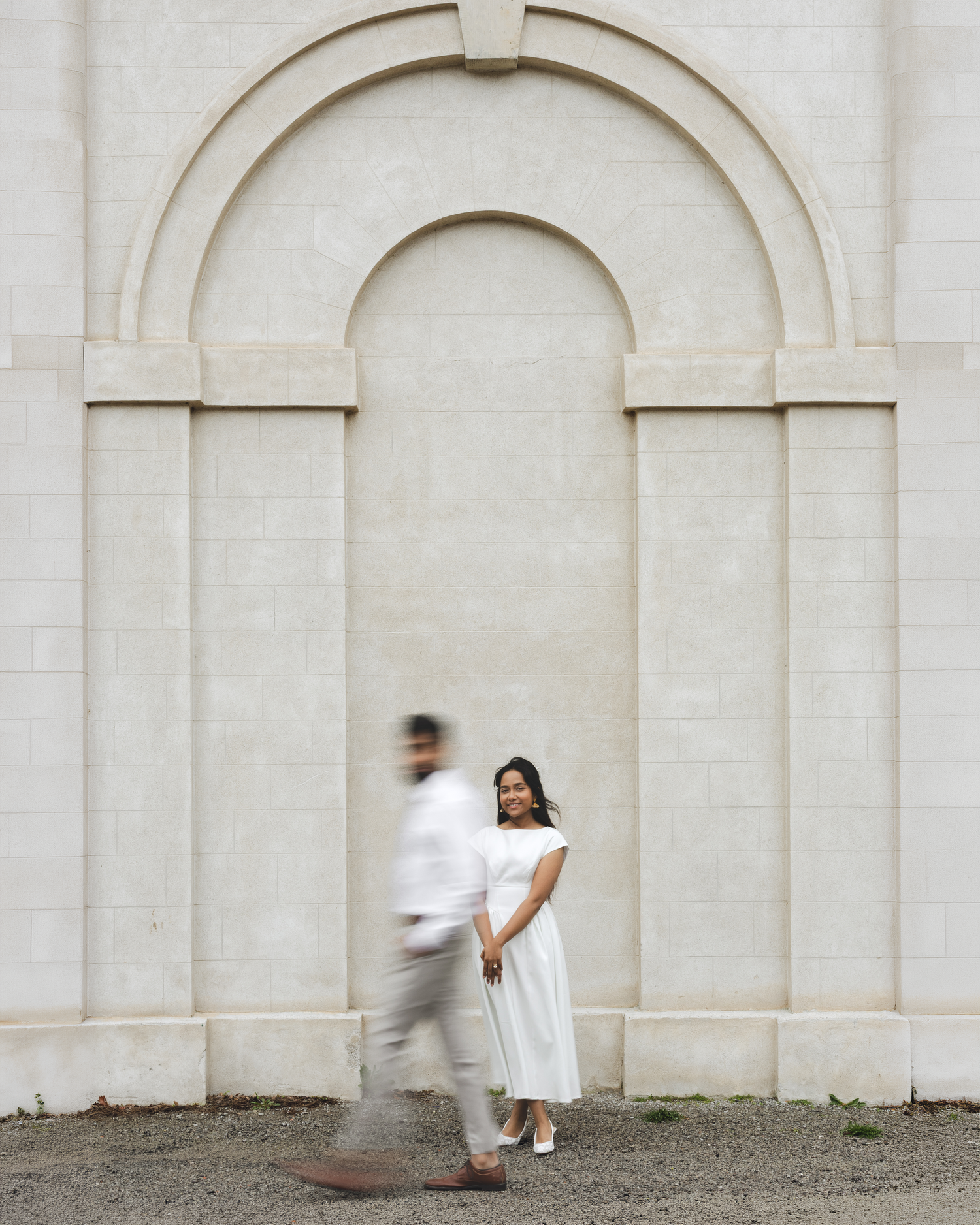 Couple in white attire posing before a colonial-style building with tall windows and pillars.