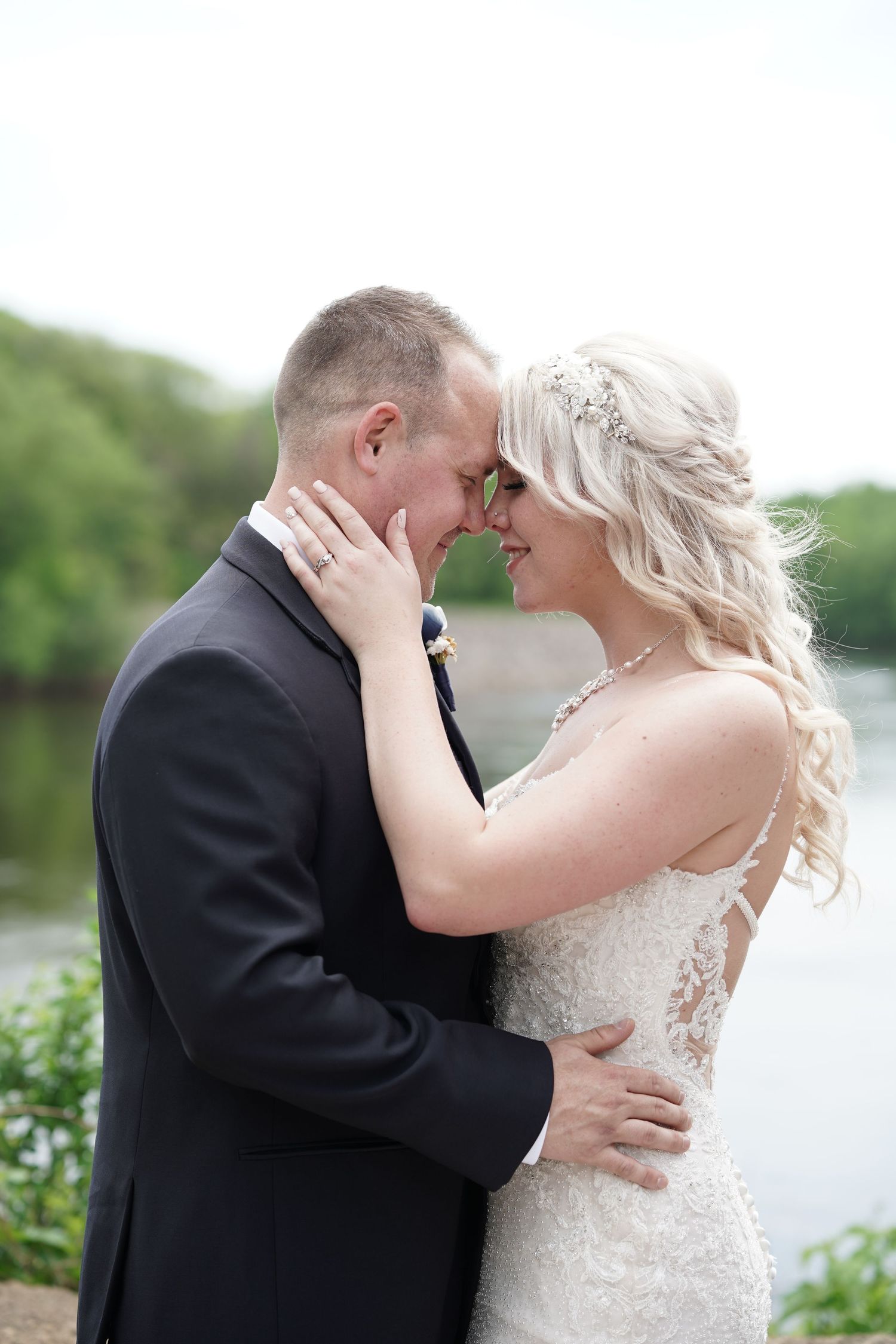 Bride and groom share a tender nose-to-nose moment by a serene lakeside on their wedding day.