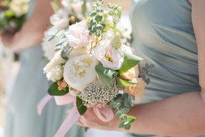 Bridesmaids in sage green dresses holding elegant bouquets of white peonies, blush roses, and eucalyptus.