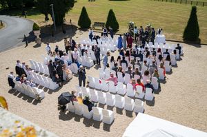 Aerial view of an outdoor wedding ceremony with white chairs arranged on a sunny gravel courtyard.