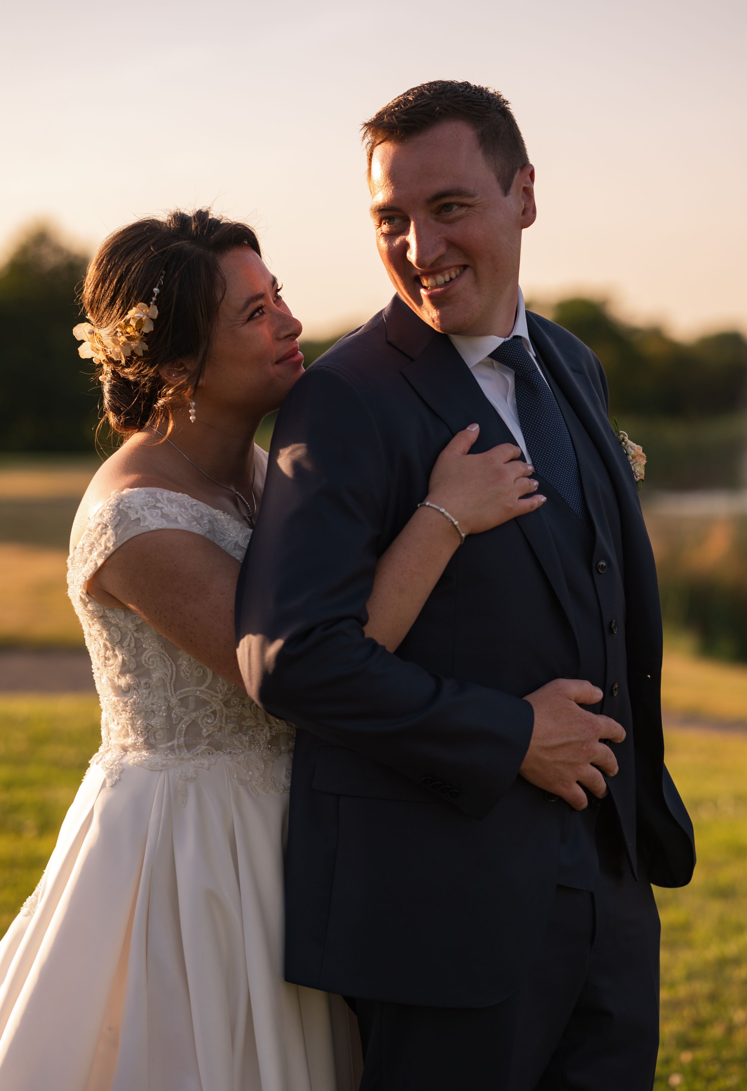 Newlywed couple sharing a tender moment at golden hour, bride in lace gown and groom in navy suit.