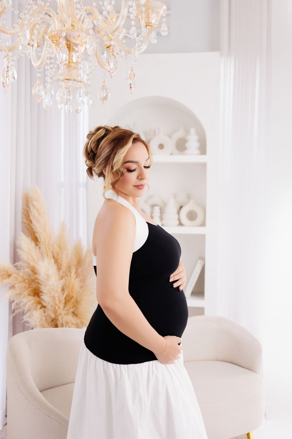 Elegant pregnant woman in black and white dress cradling baby bump in bright white luxury interior.