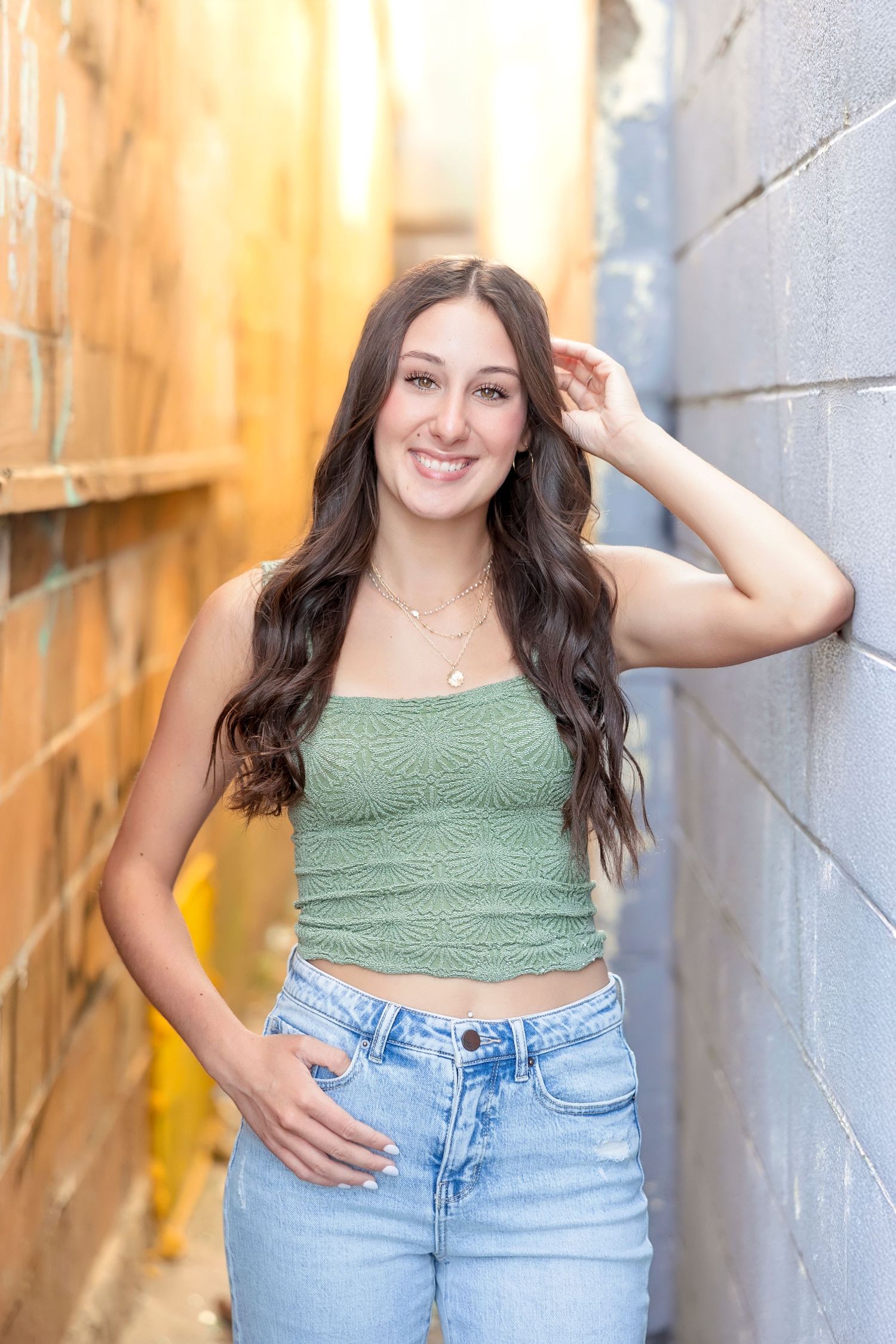 Smiling young woman in green crop top and jeans posing in an alley between brick walls.
