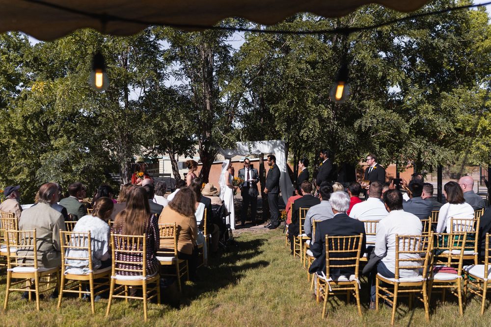 Outdoor wedding ceremony with guests seated on gold chiavari chairs under a canopy of trees in a backyard elopement