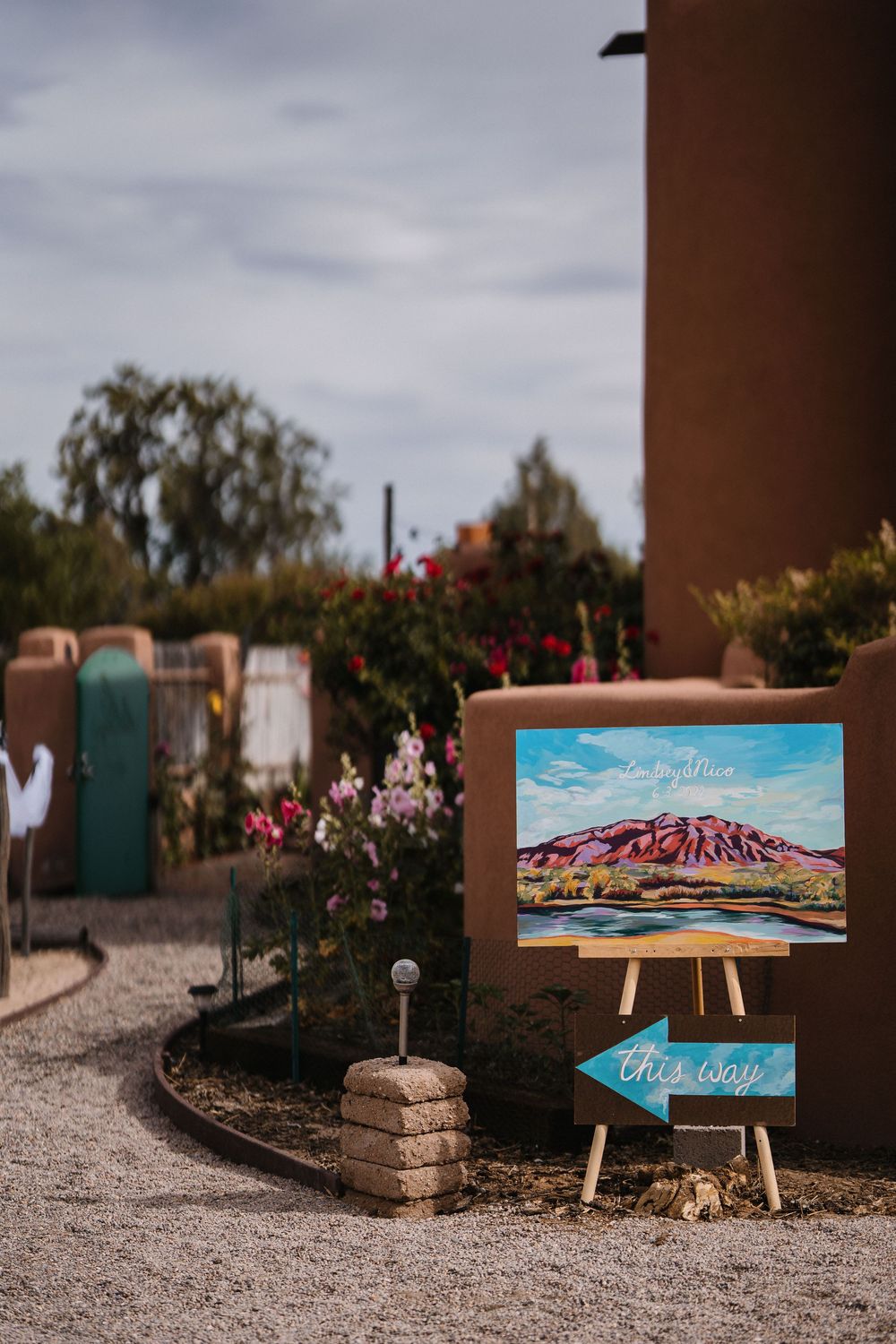 Southwest wedding venue entrance with a colorful mountain painting on an easel and a this way sign.