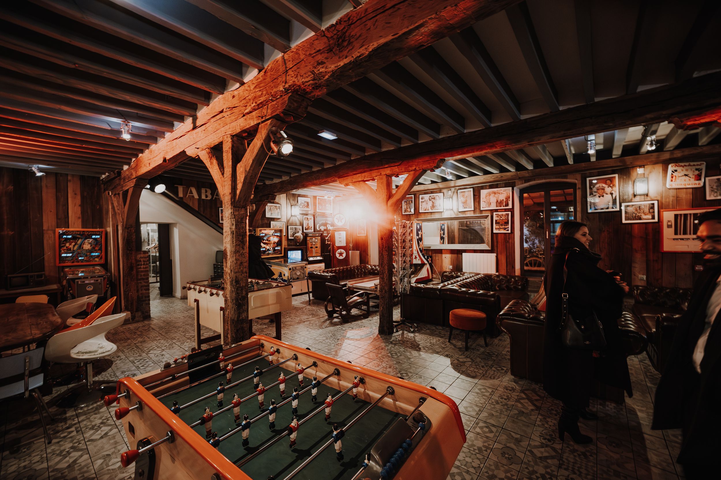 Rustic game room with foosball table, wooden beams, warm lighting, and vintage decor in a cozy bar setting.