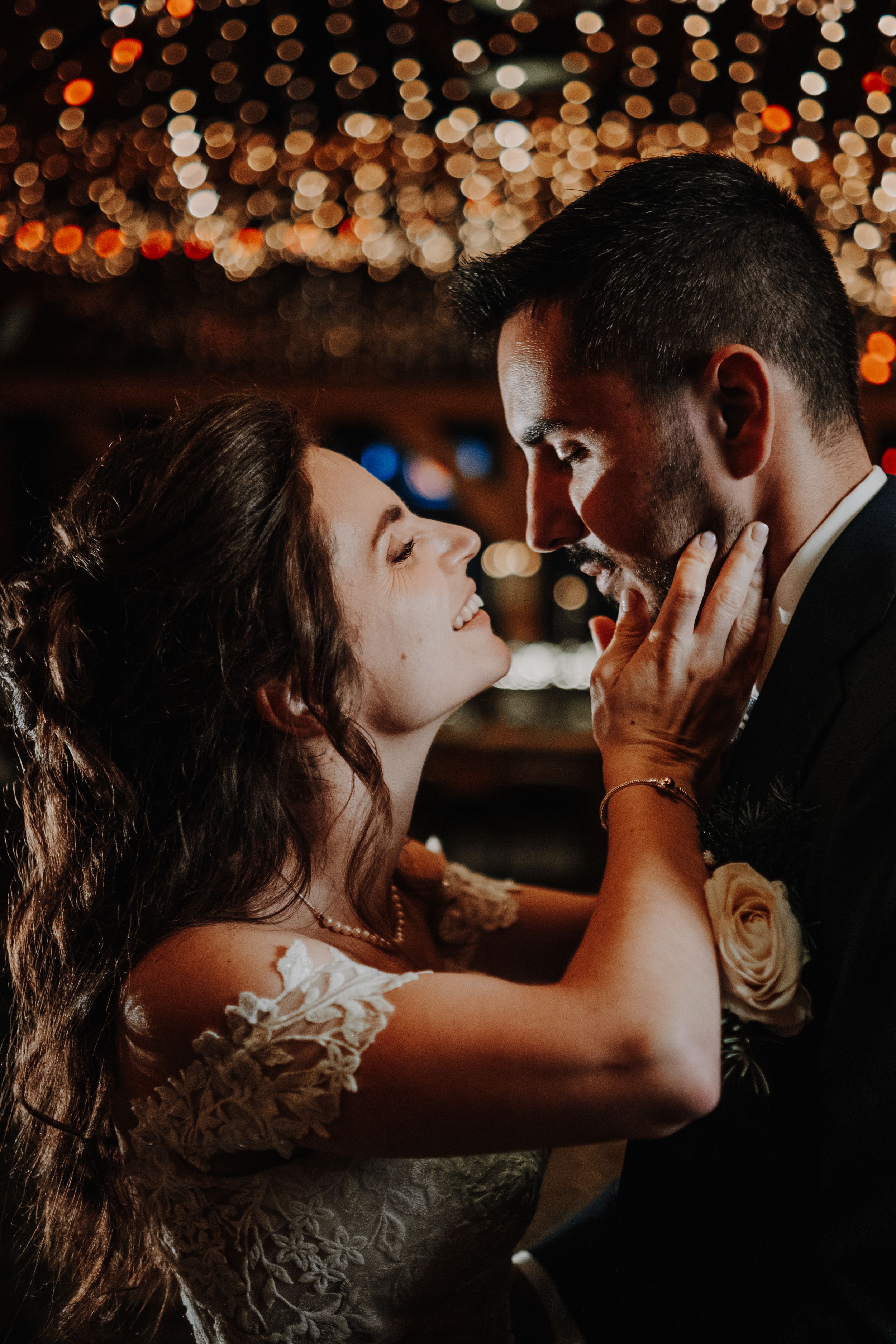 A bride and groom share a romantic moment under warm bokeh lights at their wedding reception.
