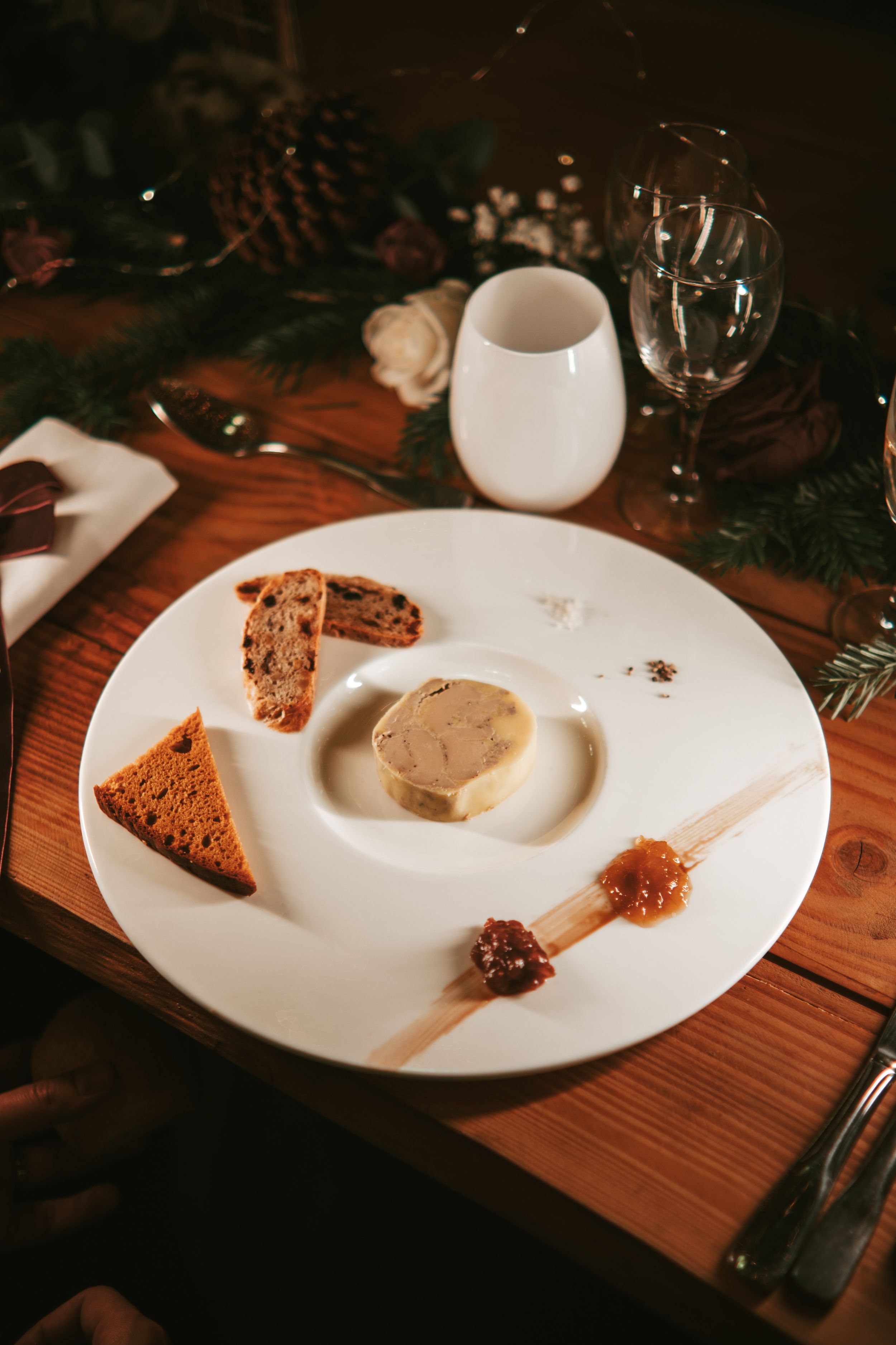 Elegant foie gras platter with toasted brioche, gingerbread, and fruit chutney on a white plate at a festive table.