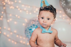 Baby boy wearing a blue party hat and bow tie during a first birthday cake smash celebration.