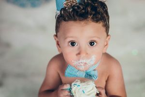 Cute baby boy eating birthday cake wearing a blue party hat and bow tie during cake smash.