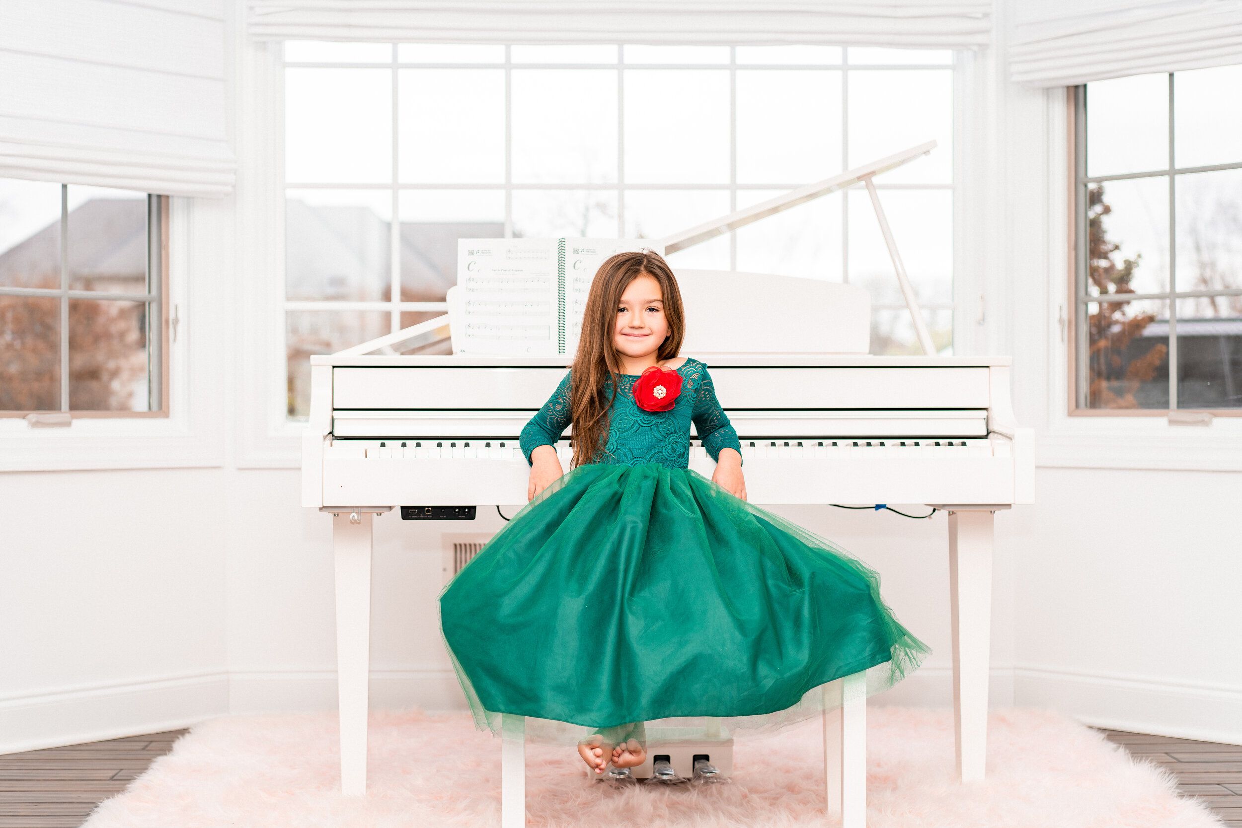Young girl in a elegant green ball gown dress posing in front of a white grand piano.