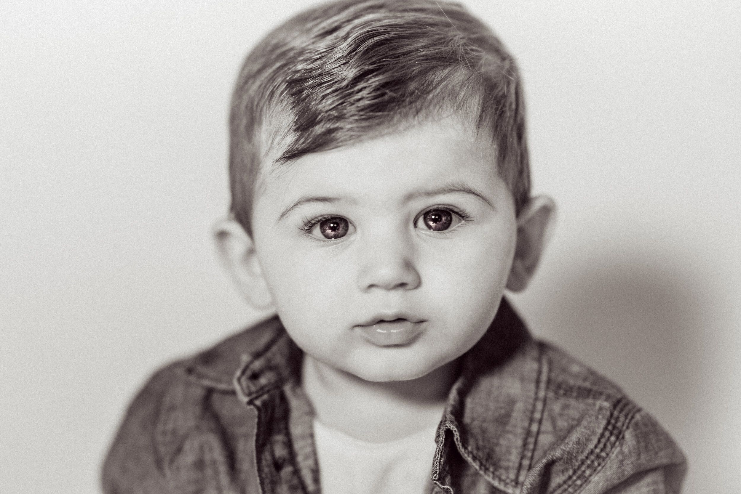 Black and white portrait of a baby boy with big brown eyes wearing a denim shirt.