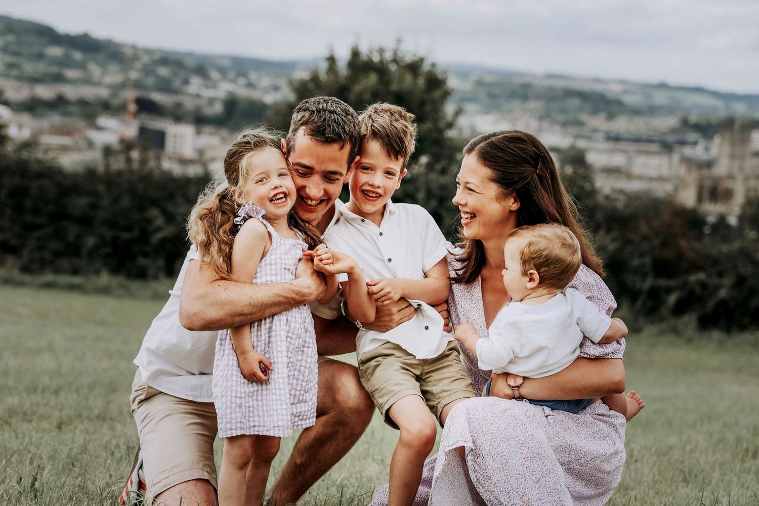 Family cuddling together with views across Bath during a relaxed outdoor family photography session.