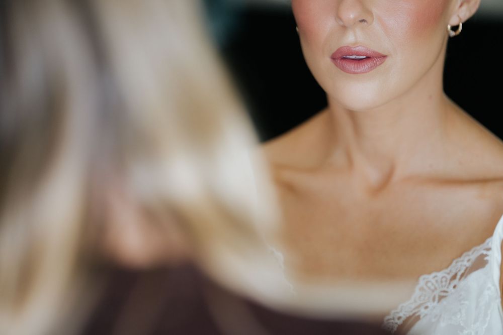 Close-up of a bride with soft pink lips, pearl earrings, and lace dress, reflected in a mirror.