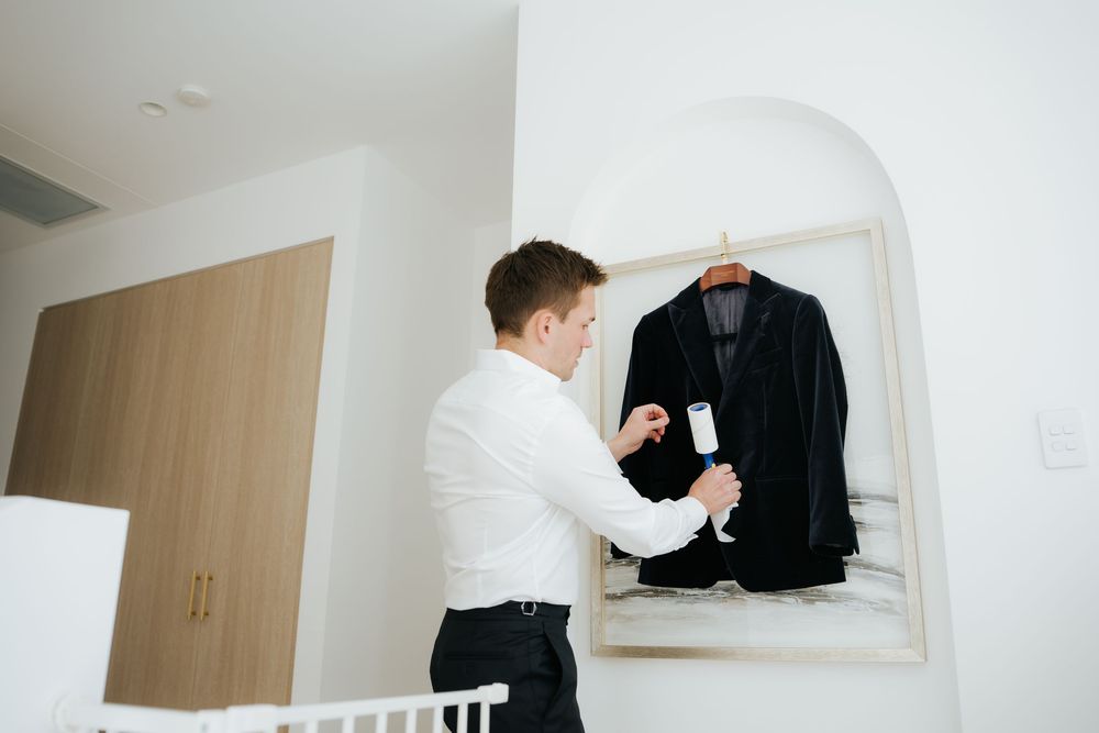 Man in white shirt steaming a black suit jacket on a hanger in a bright modern room.