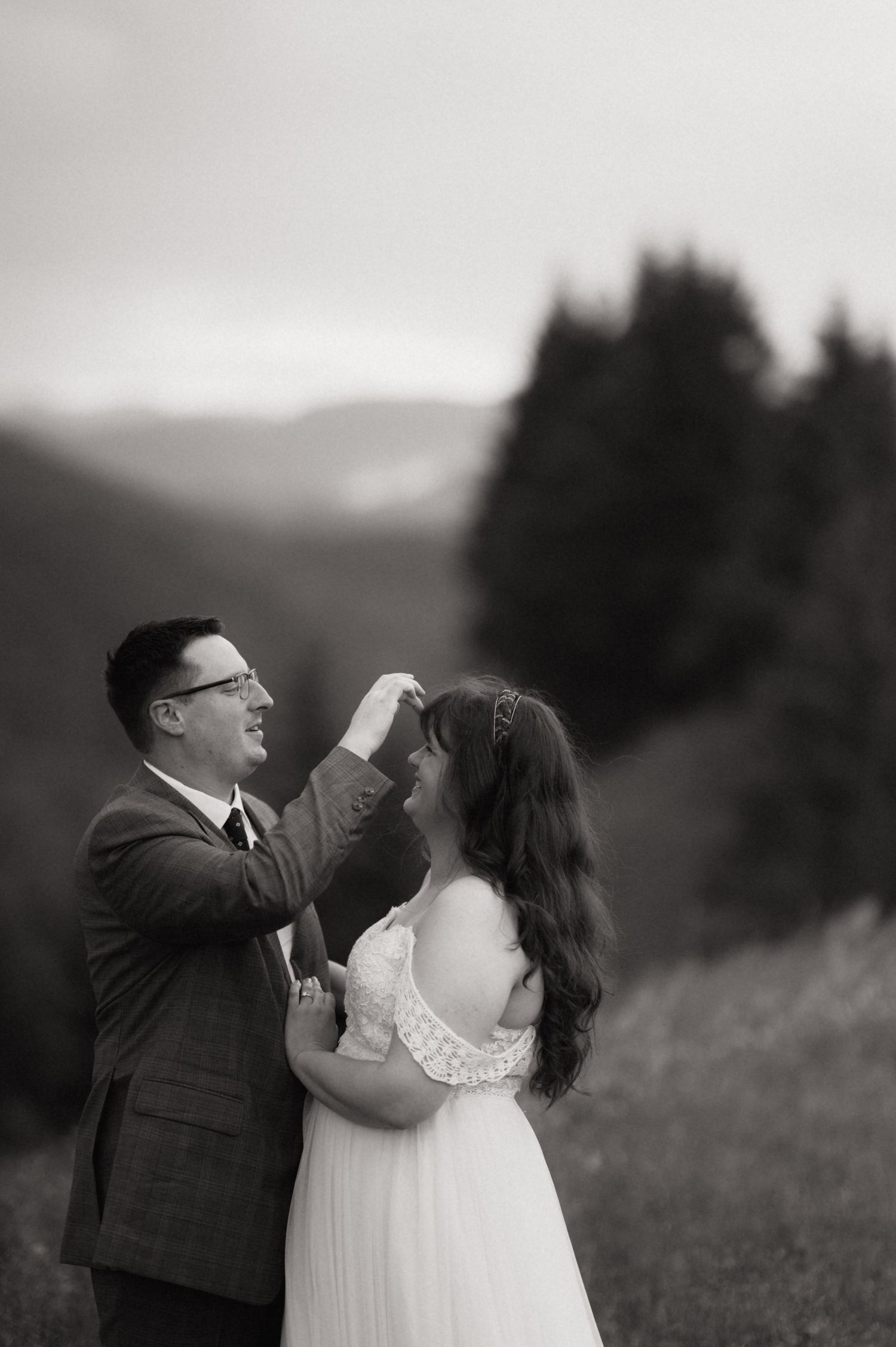 Black and white photo of a groom spinning his bride in a wedding dress outdoors with mountains in the background.