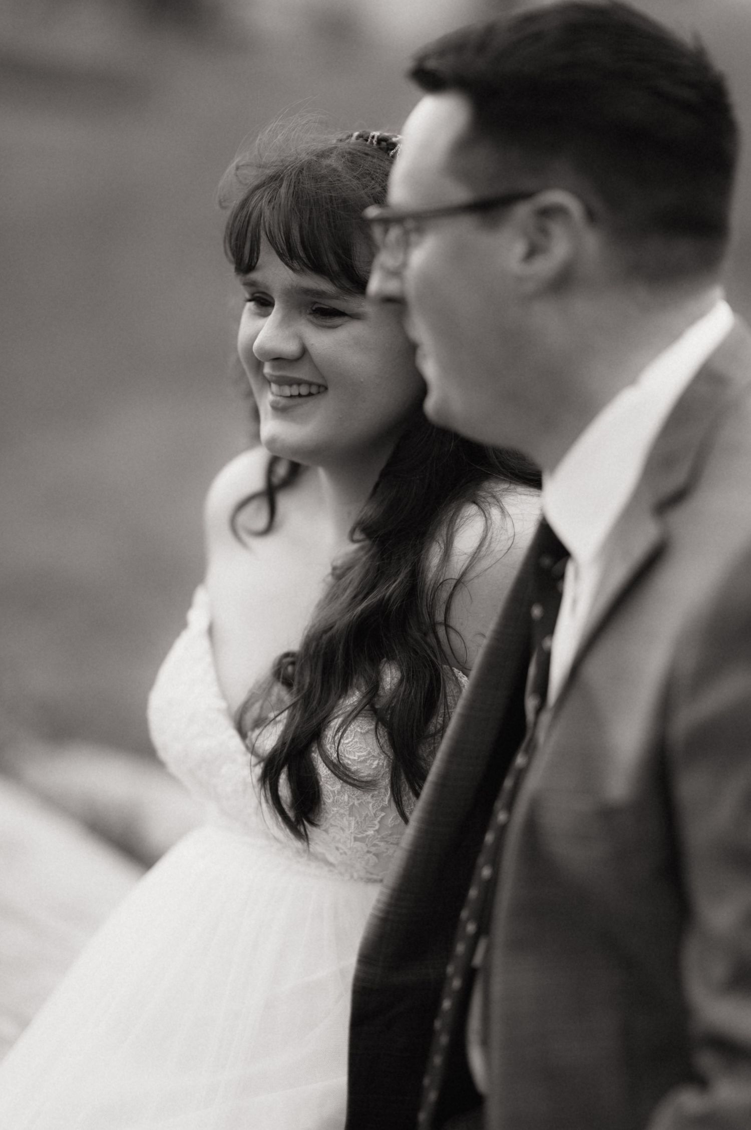 Black and white wedding photo of a smiling bride in white dress sitting beside groom in suit and tie.