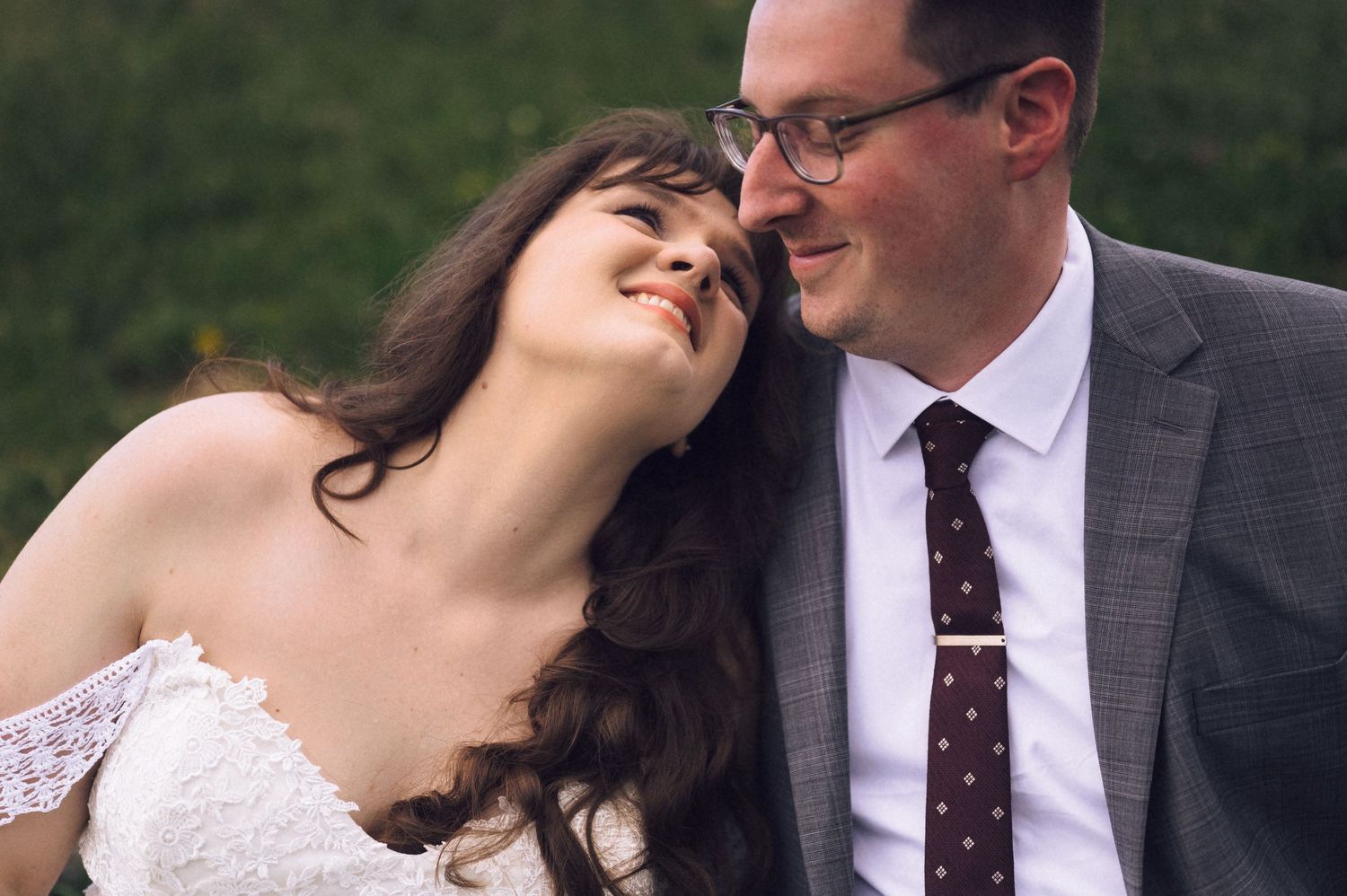 A joyful bride and groom share an intimate moment, smiling closely together outdoors on their wedding day.