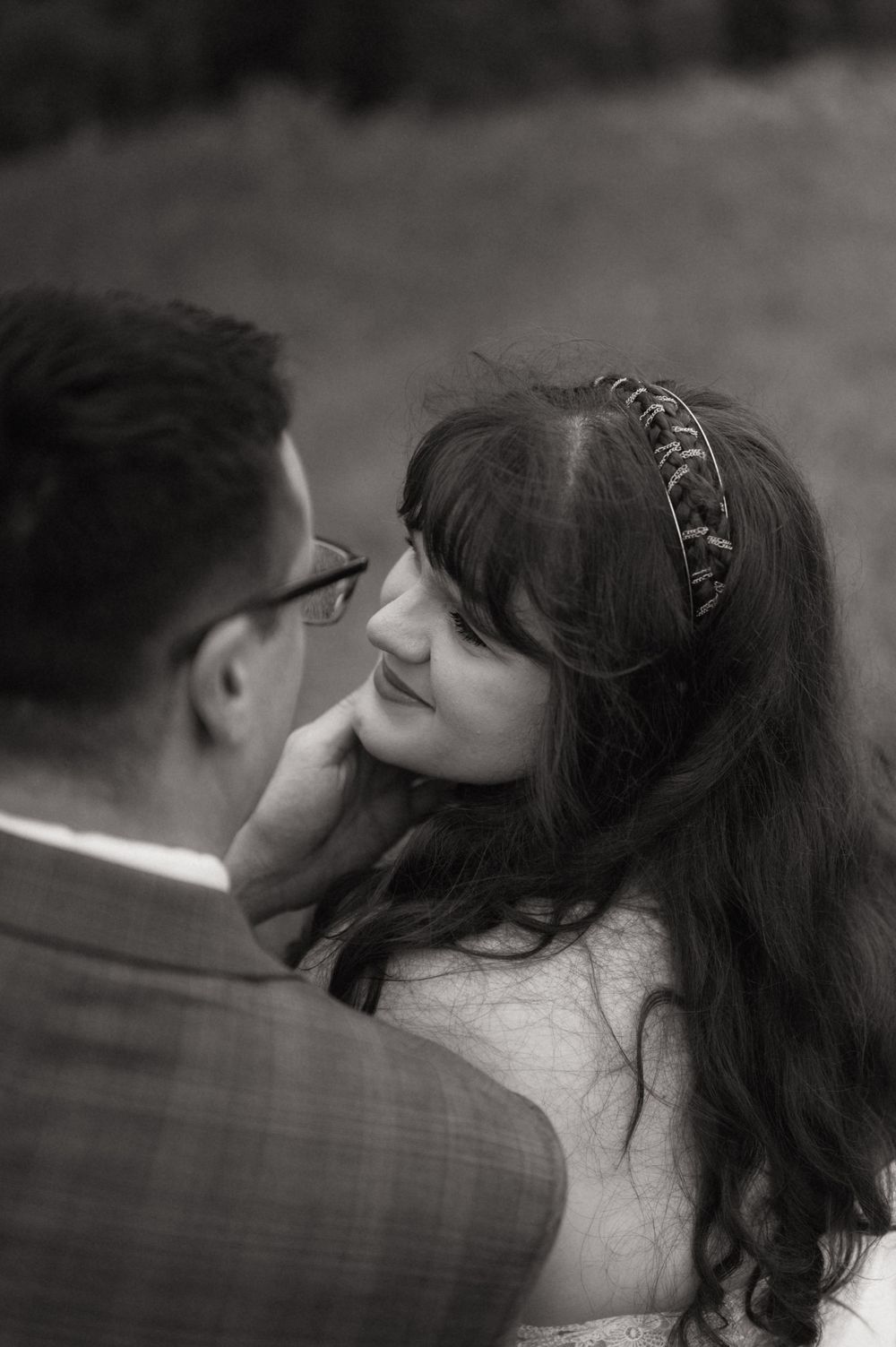 Black and white wedding photo of bride smiling up at groom, wearing a decorative headband, sharing an intimate moment.