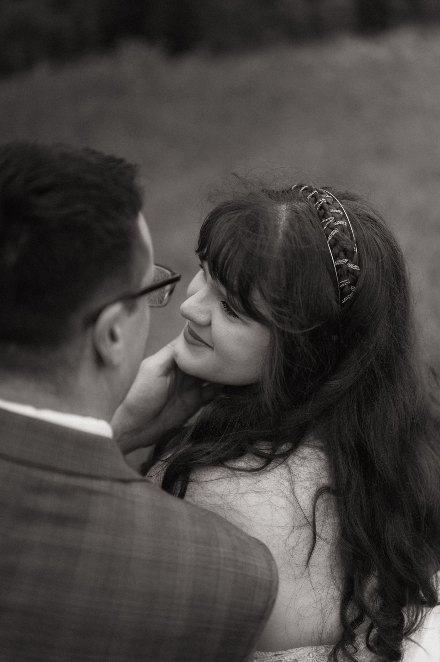 Black and white wedding photo of bride smiling up at groom, wearing a decorative headband, sharing an intimate moment.