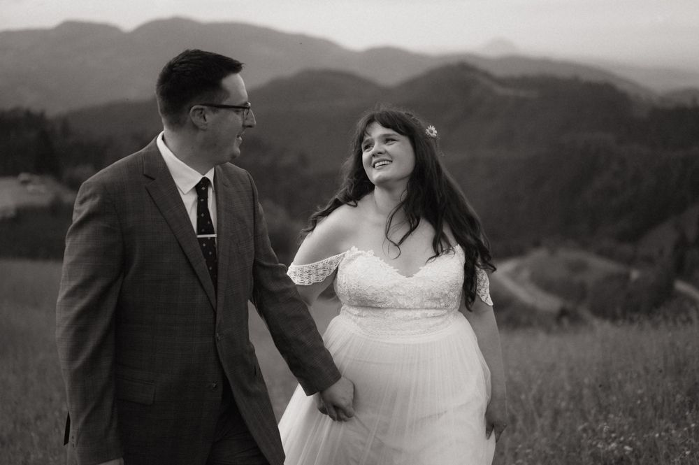 Black and white photo of a bride and groom holding hands in a mountain meadow, sharing a joyful moment.