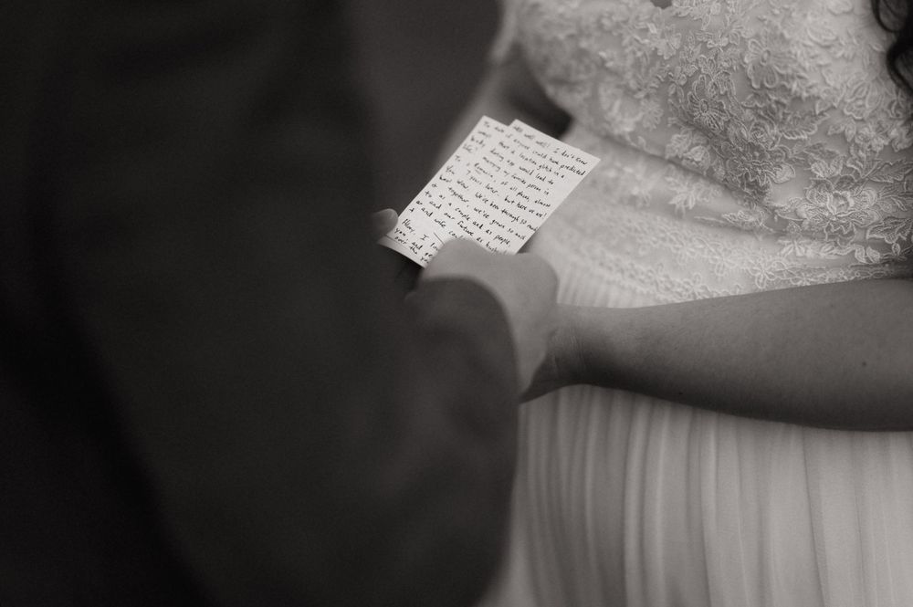 Black and white photo of a bride and groom reading handwritten wedding vows during their ceremony.