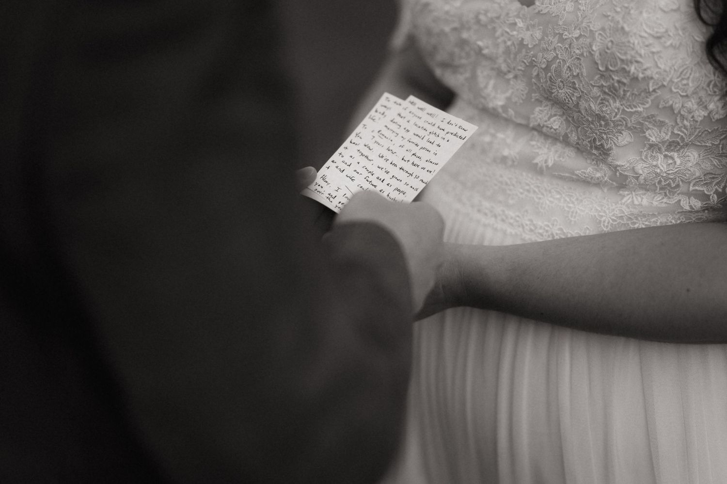 Black and white photo of a bride and groom reading handwritten wedding vows during their ceremony.