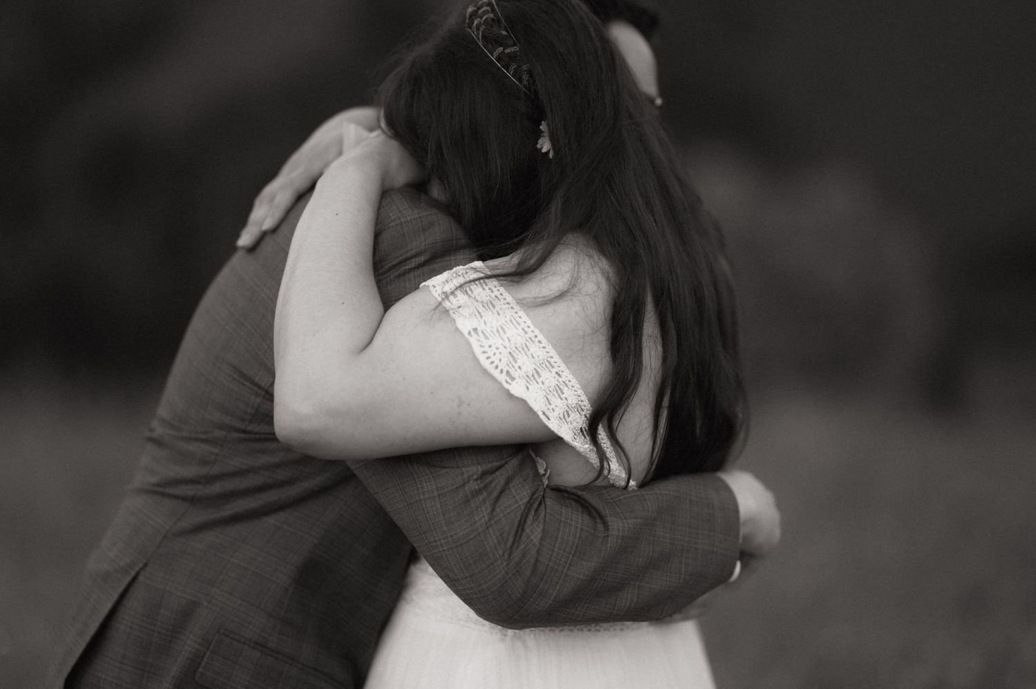 Black and white photo of a couple sharing a tender embrace outdoors, woman with long dark hair in wedding attire.