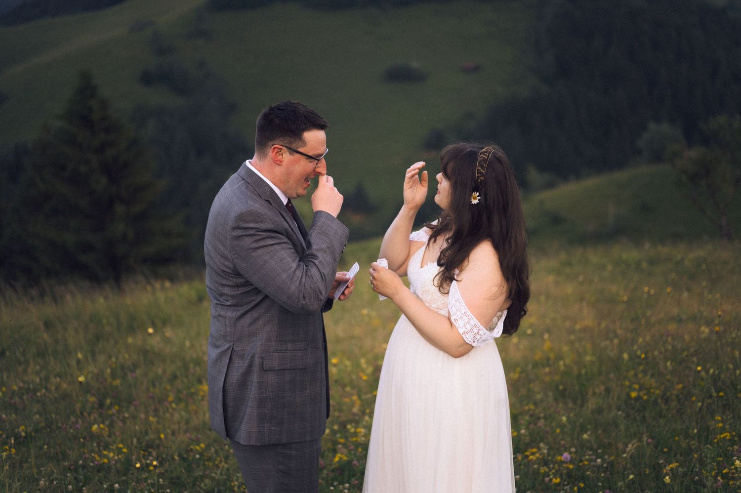 Bride and groom sharing an emotional moment in a green meadow, with rolling hills in the background during their wedding.