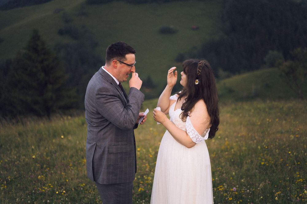 Bride and groom sharing an emotional moment in a green meadow, with rolling hills in the background during their wedding.
