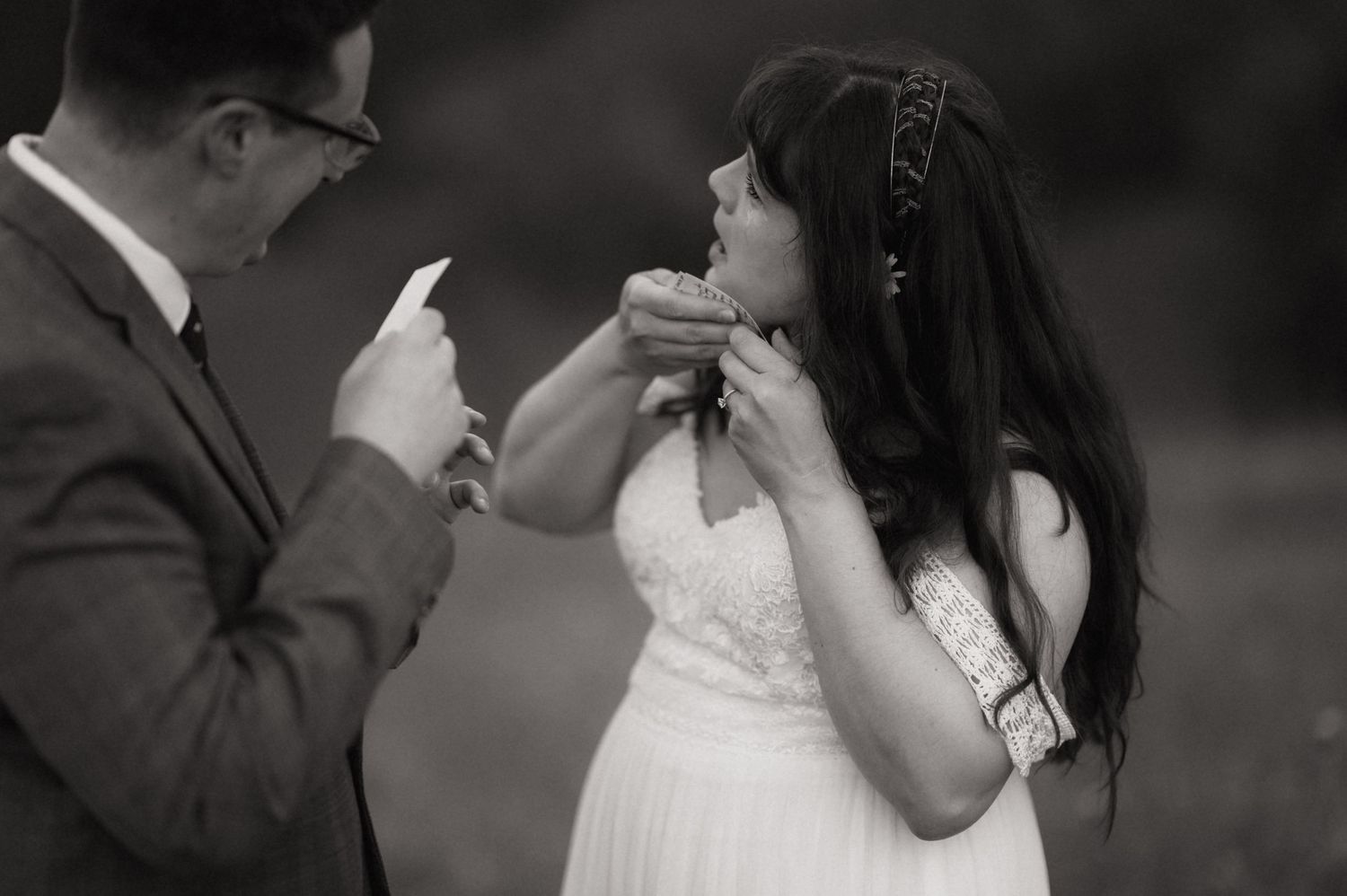 Black and white wedding photo of bride and groom exchanging rings outdoors during intimate ceremony.