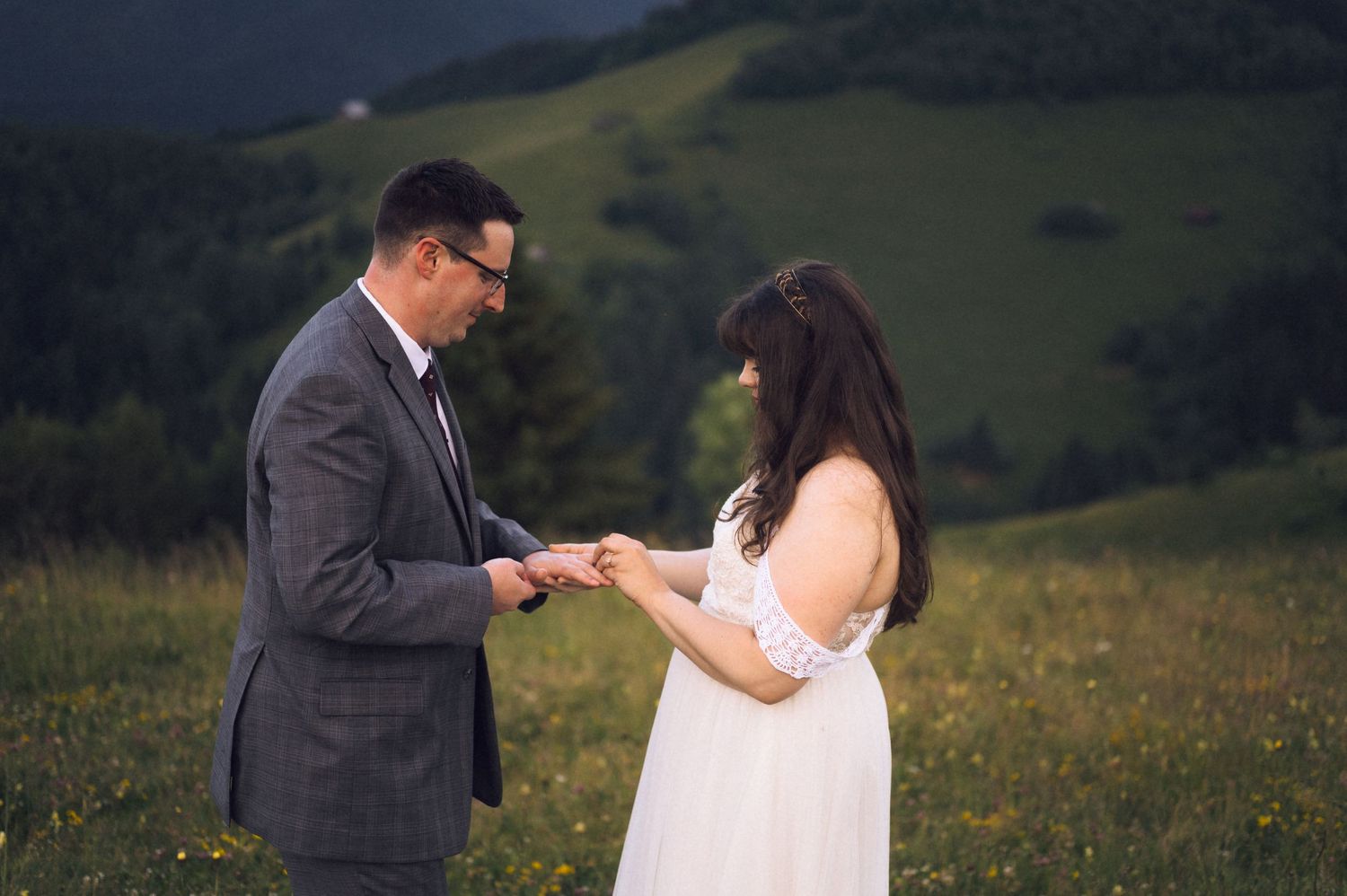 Couple exchanging rings in a lush green mountain meadow during an outdoor wedding ceremony.