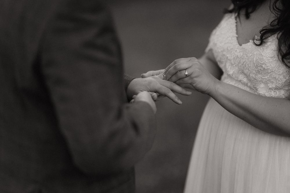 Black and white photo of a bride and groom exchanging rings during their wedding ceremony.