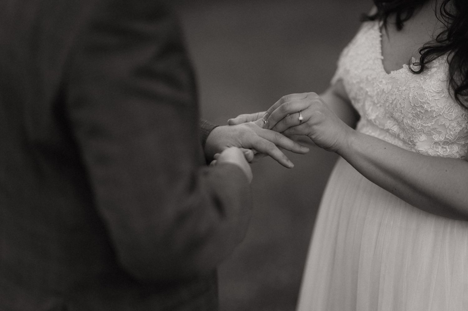 Black and white photo of a bride and groom exchanging rings during their wedding ceremony.