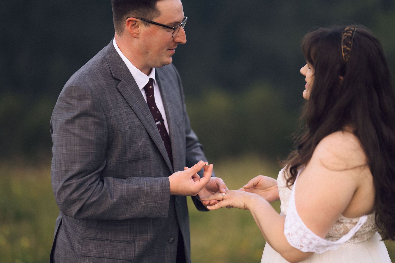 Groom placing wedding ring on bride's finger outdoors in a green field during an intimate ceremony.
