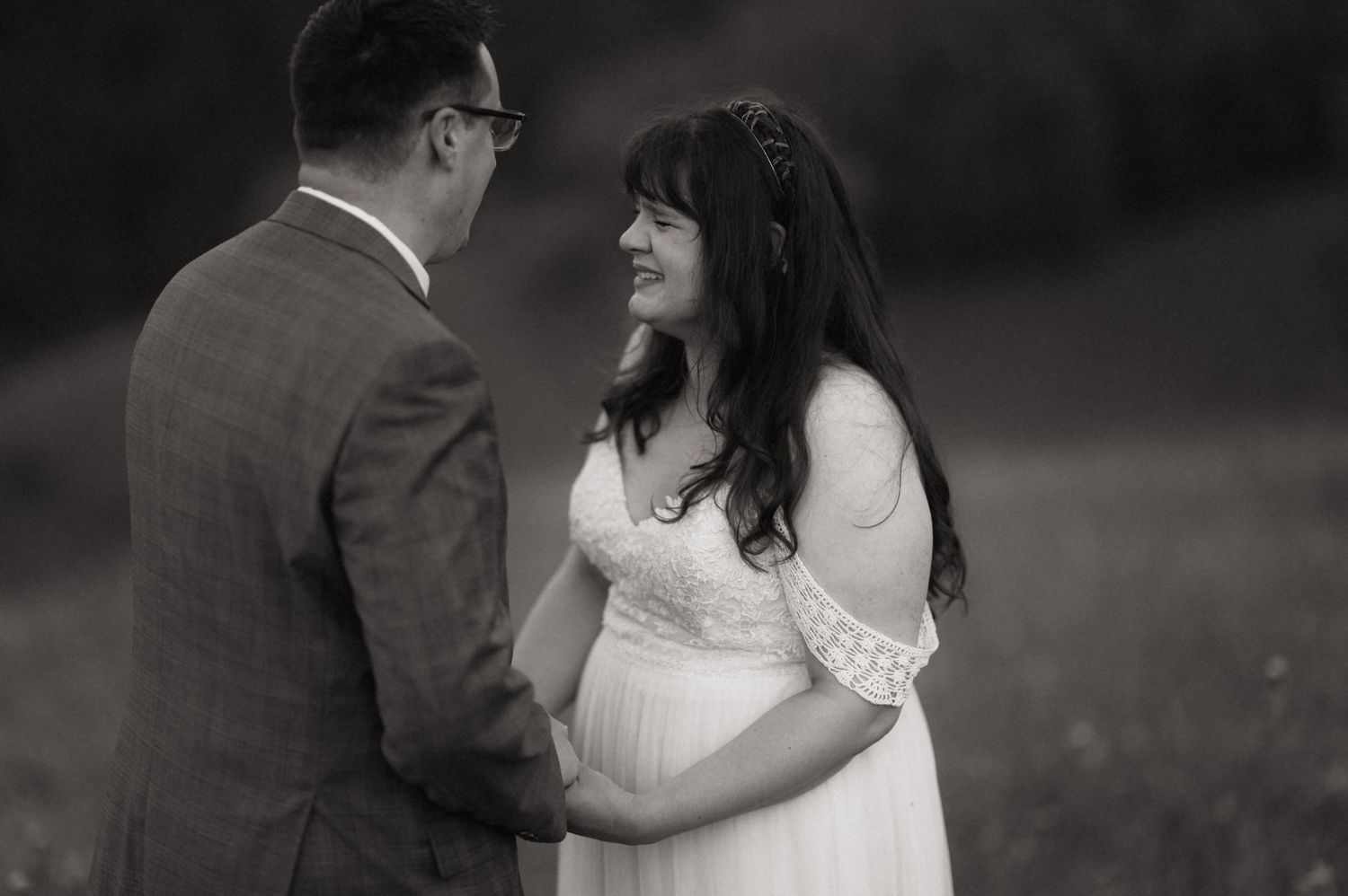 Black and white photo of a pregnant woman in white dress smiling at her partner in a field.