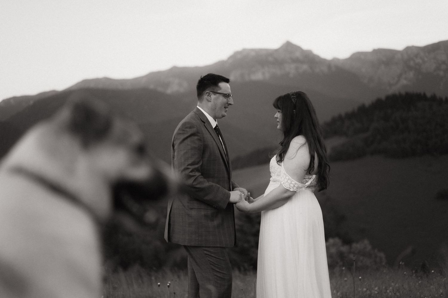 Black and white photo of a couple holding hands during outdoor wedding ceremony with mountain backdrop.