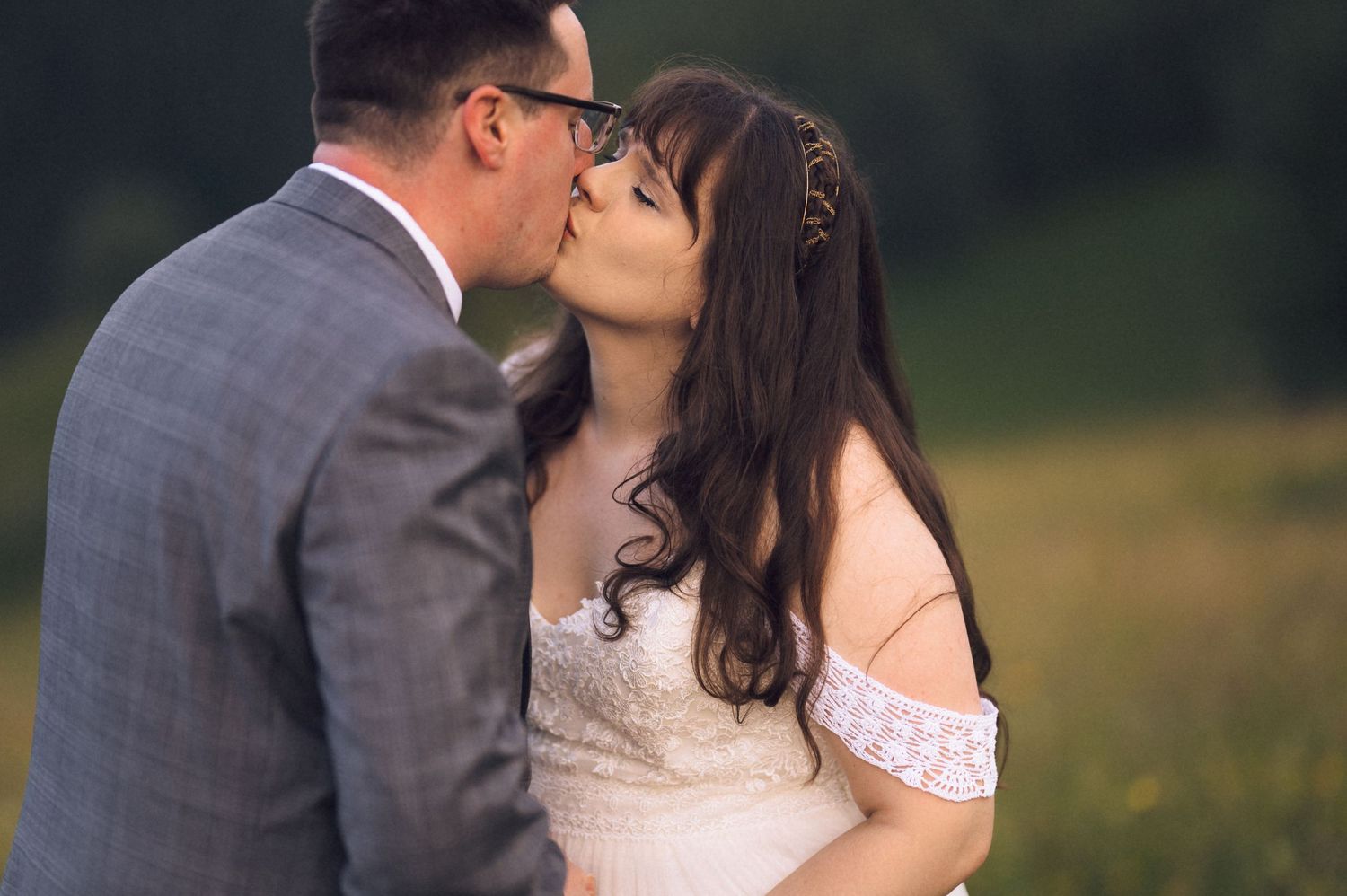Bride and groom sharing a romantic kiss outdoors in a green meadow, wedding couple portrait.