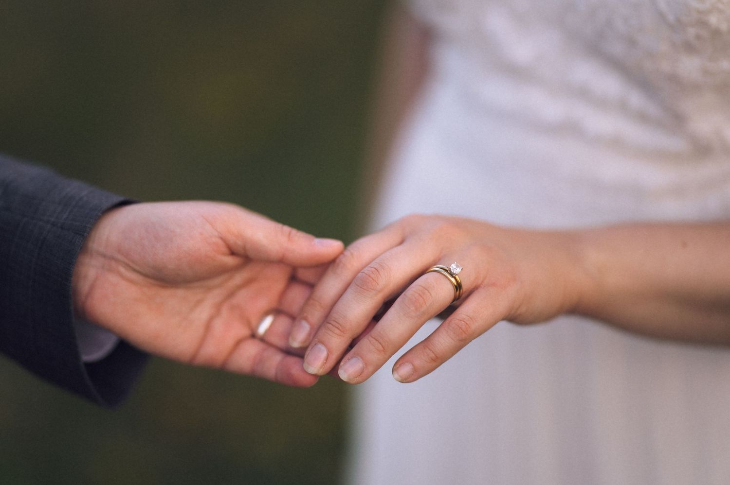 Bride and groom holding hands showing wedding rings, close-up of couple exchanging rings at wedding ceremony.