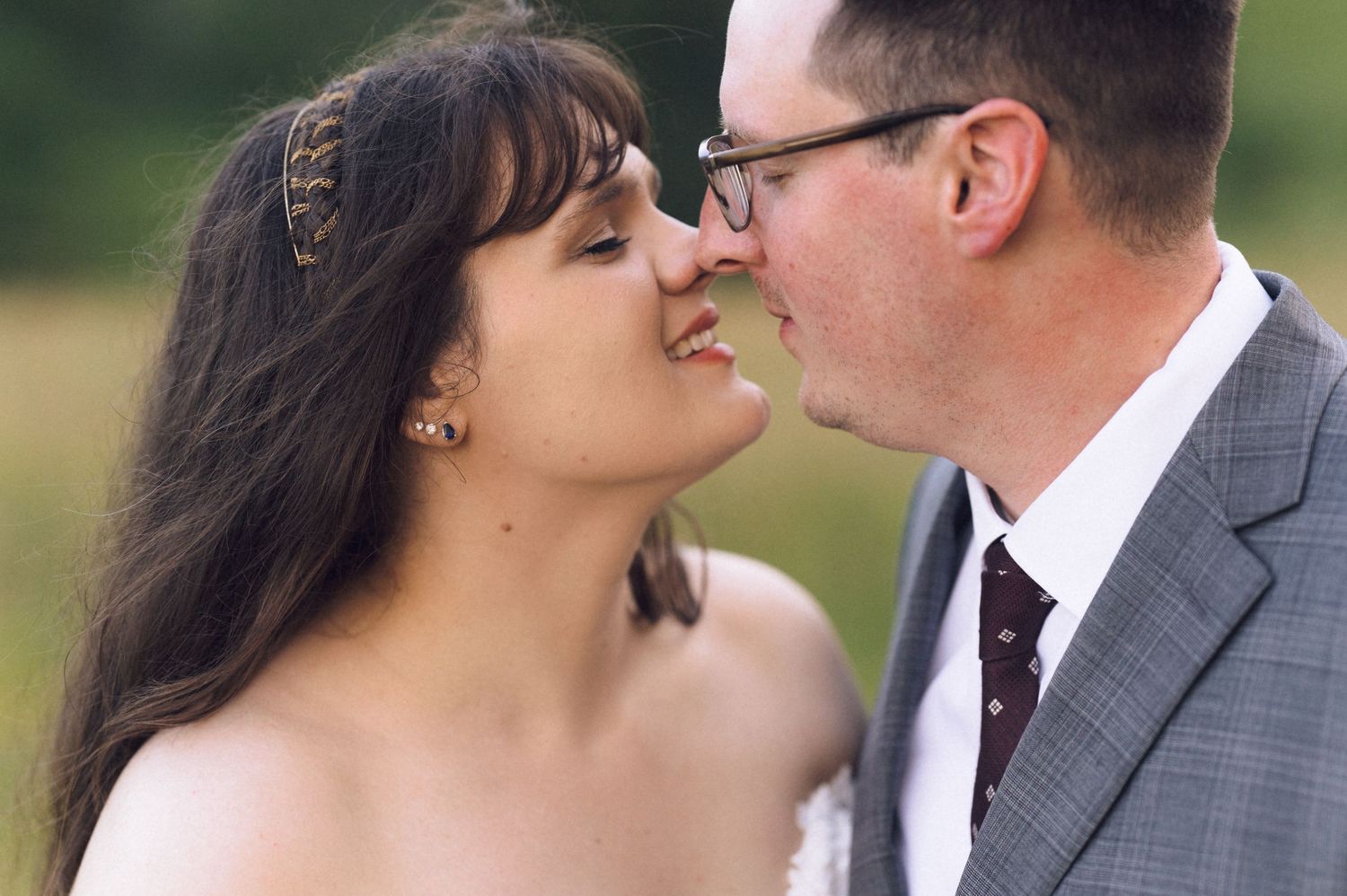 Bride and groom sharing a romantic kiss outdoors at their wedding ceremony in a lush green field.