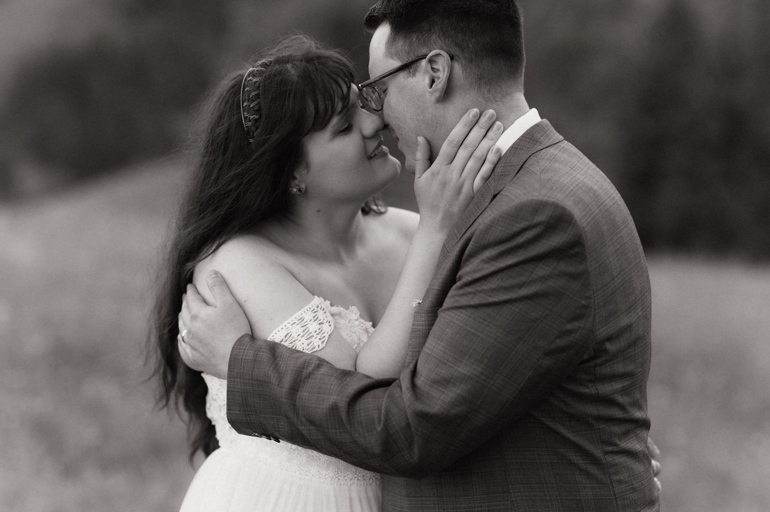 Black and white photo of a couple sharing a romantic embrace, nearly kissing, at an outdoor wedding ceremony.